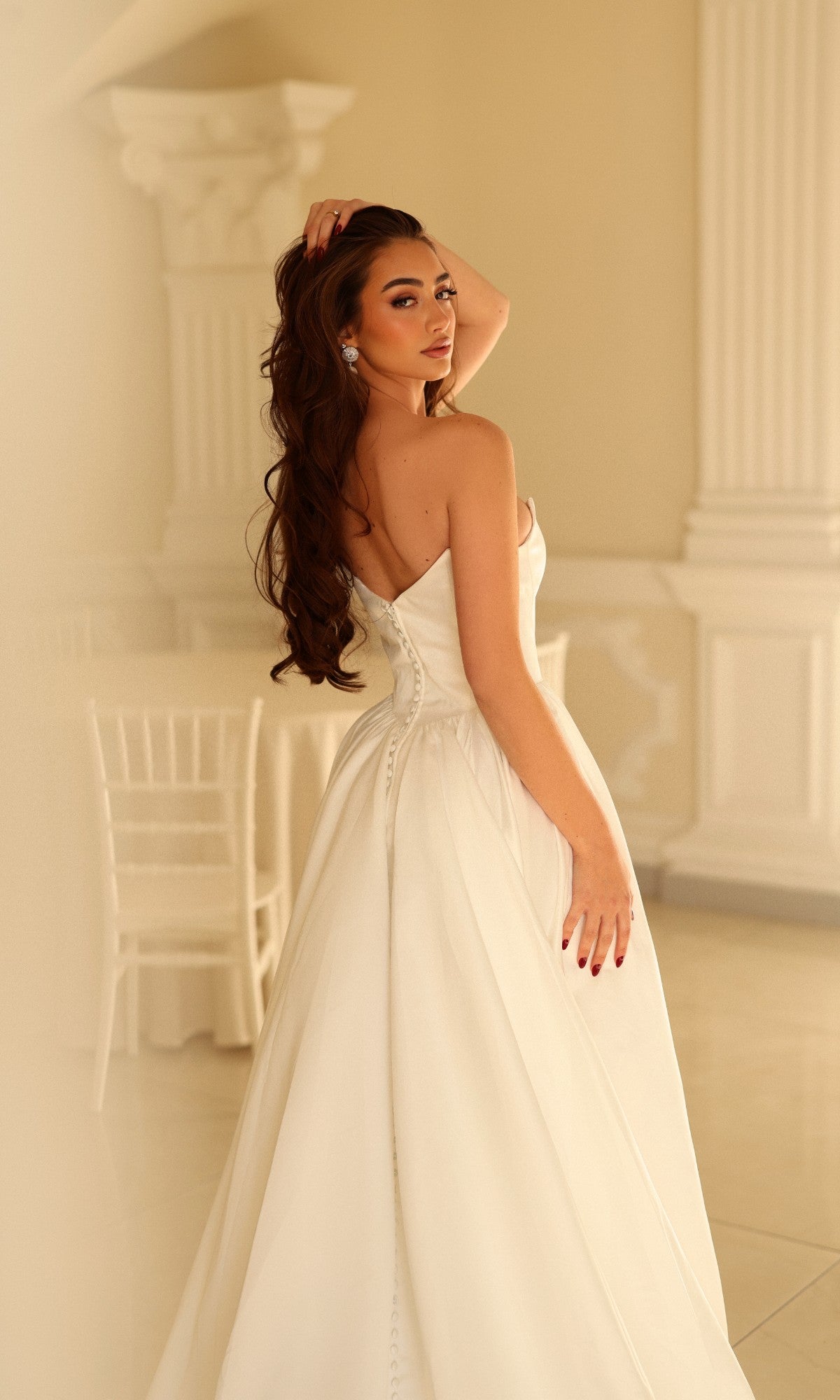 A person wearing a Long Wedding Dress: Tina Holly TW622, a strapless, floor-length white satin bridal gown with a button-up back.